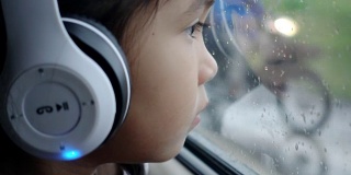亚洲漂亮的女孩听音乐耳机移动在汽车和看在雨天