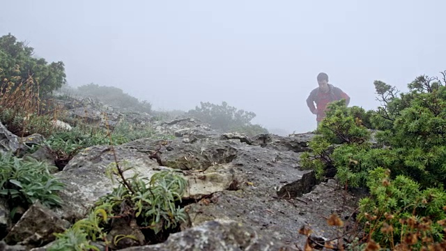 两名男性徒步者在浓雾中沿着一条布满岩石的小径爬上一座山
