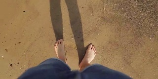 一个年轻人踩在海边金色的沙滩上。雄性的腿在海洋附近行走。光着脚的人在沙滩上海浪。暑假或假期。