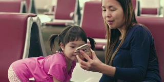 亚洲年轻的母亲和女儿在候机楼登机口用智能手机等待