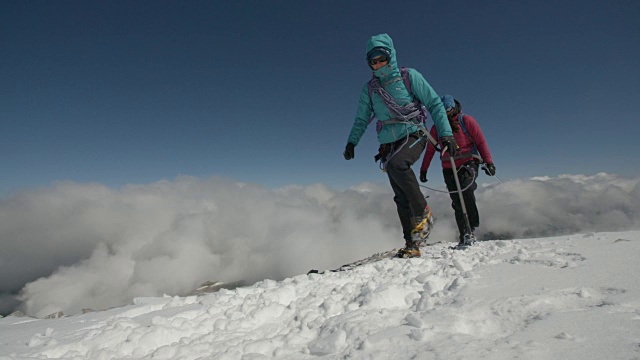 两名女登山家穿越云层上方的冰雪，以抵御寒冷。