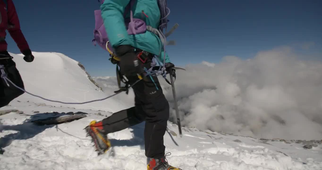 在慢镜头中，两个女人用冰镐和冰爪爬山。