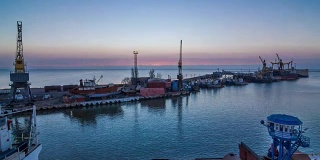日出时，一艘载有拖轮的大船进入港口。一个在亚速海拥有货物起重机和铁路集装箱货车的工业海港码头。间隔拍摄FullHD视频