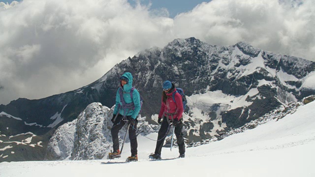 两名女登山运动员穿过高山中的冰川山脊，风暴云正在酝酿。