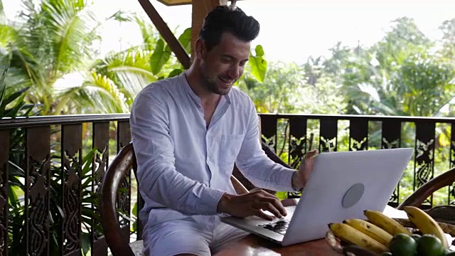 快乐微笑的男人在阳台上使用笔记本电脑，休闲商人在户外用电脑打字