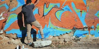 涂鸦艺术家在华尔街墙上作画。帅哥用喷雾器喷瓶喷彩色涂料，都市户外艺术概念。缓慢的运动。后视图，总体规划