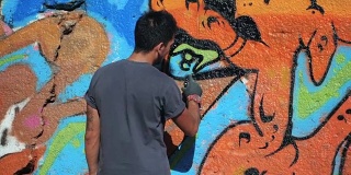 涂鸦艺术家用气溶胶作画。拿着喷雾器的人。缓慢的运动。年轻的城市画家在夏日的阳光下，在城市的街道墙上画上五颜六色的涂鸦