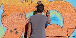 英俊的天才小男孩用喷雾剂在城市的街道墙上涂鸦。电影色调的慢动作镜头。创造性的艺术。后视图，总体规划