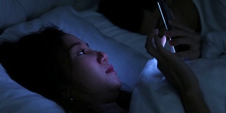 年轻女子晚上躺在床上玩智能手机