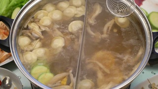 概念火锅家庭烹饪。从沸腾的汤中取出玉米、蘑菇和饺子视频素材模板下载