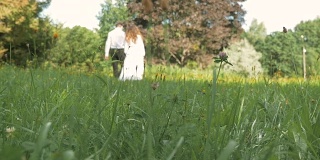 一位年轻女子和一位身穿白色西装的男子在公园里散步。牵手，在模糊地带。