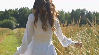 一位穿着白色衣服的妇女正沿着麦田走着。慢动作视频素材模板下载