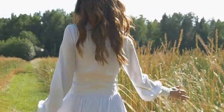 一位穿着白色衣服的妇女正沿着麦田走着。慢动作