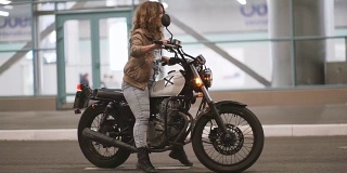这个骄傲美丽的女孩把她的摩托车转过来，坐在上面，在夜晚的街道上骑车离开