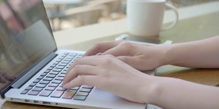 亚洲年轻女子在一个咖啡馆打电话，看着她的笔记本电脑屏幕在她的咖啡休息时间