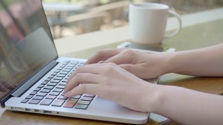 亚洲年轻女子在一个咖啡馆打电话，看着她的笔记本电脑屏幕在她的咖啡休息时间视频素材模板下载