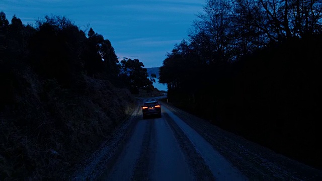 鸟瞰图汽车行驶在乡村道路上，SUV驾驶在黄昏与前灯穿过松树