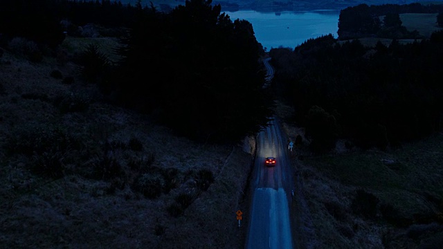 鸟瞰图汽车行驶在乡村道路上，SUV驾驶在黄昏与前灯穿过松树