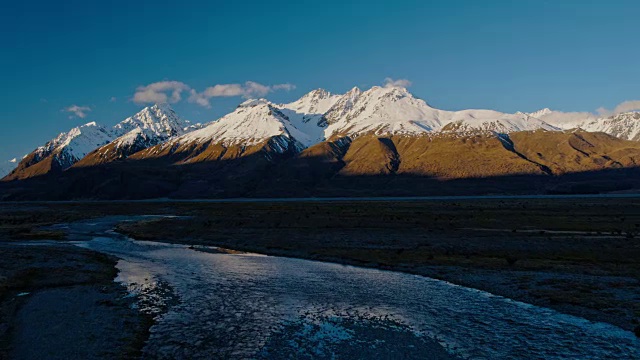 鸟瞰图飞过雪融化的河流，朝向新西兰雪山的山峰