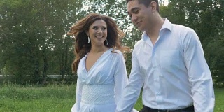 一位年轻女子和一位身穿白色西装的男子在公园里散步。牵手，在模糊地带。