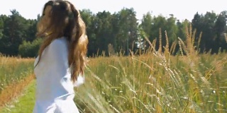 一个年轻漂亮的女人穿着白裙子在麦田里纺纱。缓慢的运动。