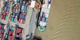 Commercial port with container ships during loading and unloading, and a container ship pulled by tugboats