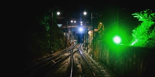 现代无人驾驶的地铁列车向前疾驰，沿着马来西亚的夜幕，地上的铁路，夜晚明亮的路灯。1920 x1080