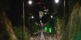 现代无人驾驶的地铁列车向前疾驰，沿着马来西亚的夜幕，地上的铁路，夜晚明亮的路灯。1920 x1080