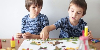 可爱的小朋友们，男孩子们，在学校里一边用胶水涂树叶，一边做工艺品，秋天的时候