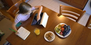 一个六岁的小女孩在笔记本上写字，在平板电脑上浏览