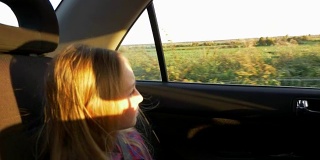 年轻的白人女孩看着车窗开车。日落夏秋黄昏。金色的夕阳。