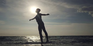 年轻女子在休闲风格-牛仔和黑色上衣在海滩上做芭蕾。迷人的芭蕾舞演员在秋天的沙滩上练习伸展。慢动作