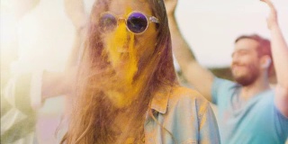一个美丽的金发女孩在胡里节与她的朋友跳舞的特写肖像。她的脸上和衣服上都涂满了彩色的粉末。人们在背景中跳舞。