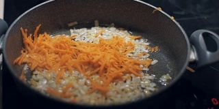 厨师将切碎的胡萝卜与洋葱和葵花籽油一起放入煎锅中。慢动作