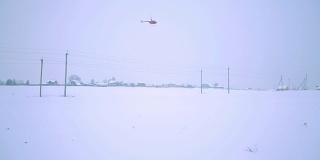 一架红色的直升机正飞过田野和电线。从地面射击。