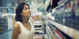 年轻的亚洲女士在超市选择酒精饮料