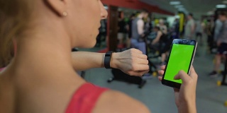 活跃的女士正在检查手腕上的健身追踪器，并与智能手机应用同步