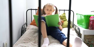 小女孩坐在床上读她的课本