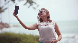 年轻女子戴着太阳镜用智能手机自拍，在海上旅行。1920 x1080视频素材模板下载