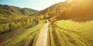 空中FHD全高清视图。在阳光明媚的夏日清晨，低空飞过山区乡村土路和草地。附近有绿树，阳光和山河