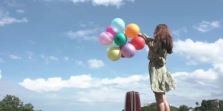 一个美丽的女孩在户外拿着一个气球，背景是山脉和河流。想想亚洲女孩的开朗。