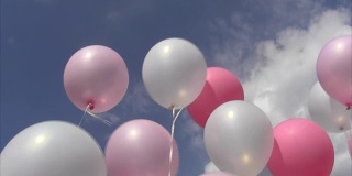 粉红色和白色的充气球在线上随风摆动着对着天空和云朵