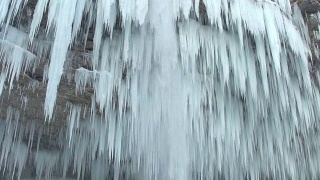 近距离观察:山上的河流瀑布在冬天结冰成许多白色的冰柱视频素材模板下载