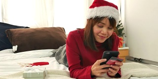 亚洲女人放松与她的智能手机和网上购物在圣诞节活动