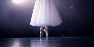 白色芭蕾舞演员的腿后面是一个黑色的舞台。