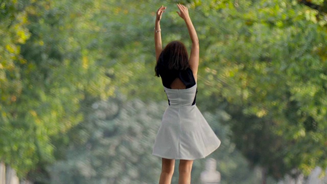 穿着裙子的黑发女孩在公园里快乐地打转，手在空中