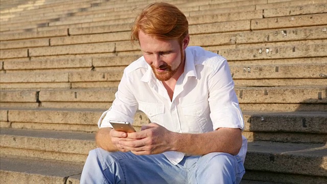 一个年轻人拿着智能手机坐在城市的楼梯上