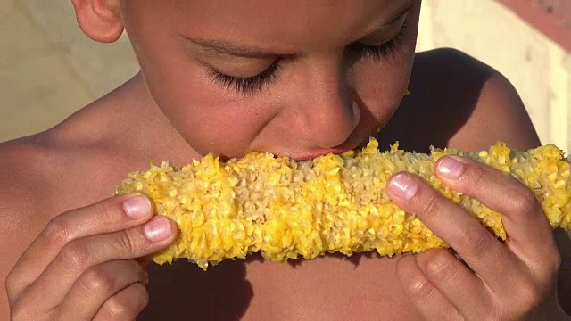 饥饿的难民小男孩正在吃玉米棒子。注意煮熟的玉米
