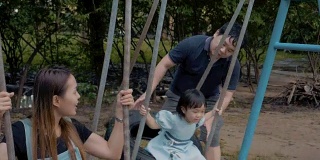 亚洲家庭与一个小女孩荡秋千享受在公共公园