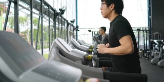 两个男人在跑步机上跑步，在健身房做有氧运动